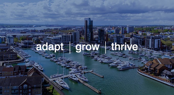 Drone image of water, boats, buildings and sky rise buildings. Image taken on a sunny day with white clouds. The text 'adapt | grow | thrive' is in front of the drone image in white writing.