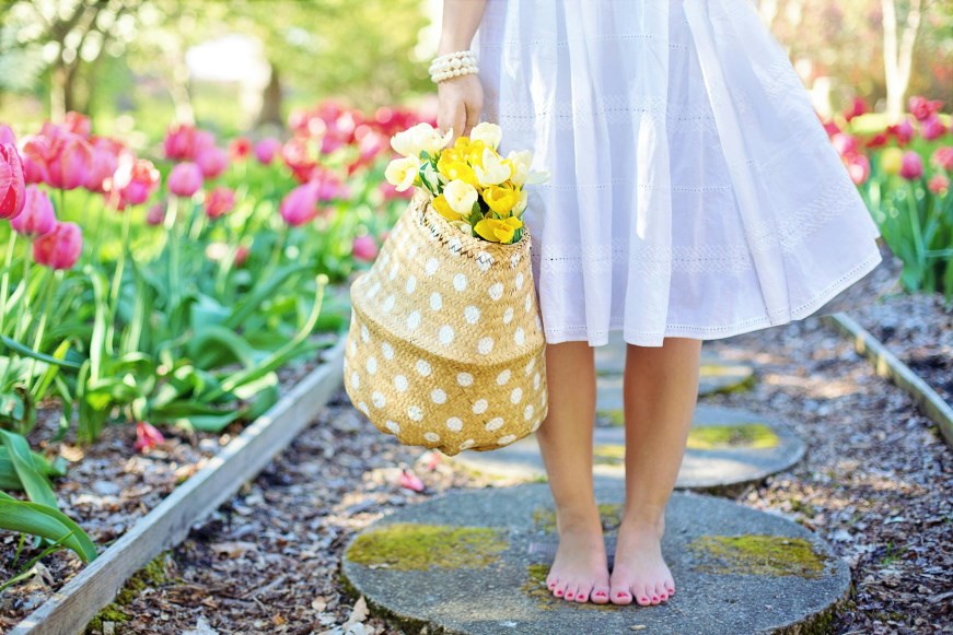 A girl standing on a path surrounded by, and carrying, flowers