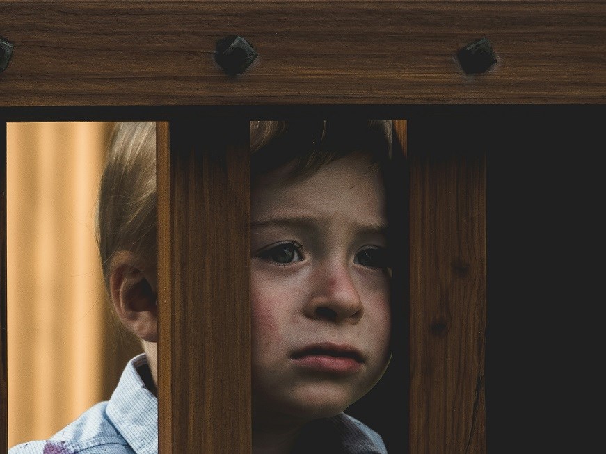 Sad child peering through railings