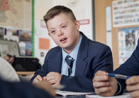 A child with Down's syndrome, dressed in a school uniform, sitting in a classroom